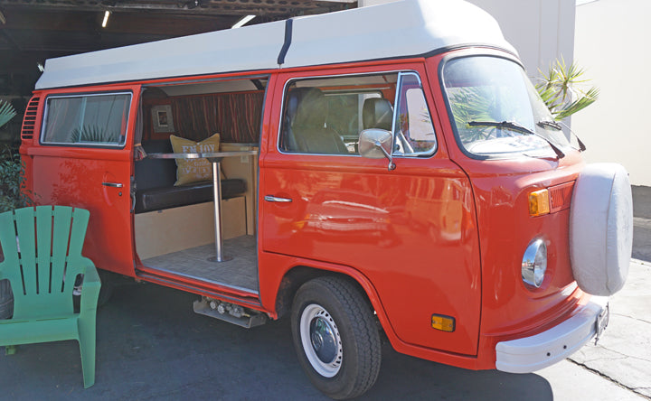 Vintage red VW camper van RV rental with pop-top, side door open revealing cozy interior. Perfect for road trips!