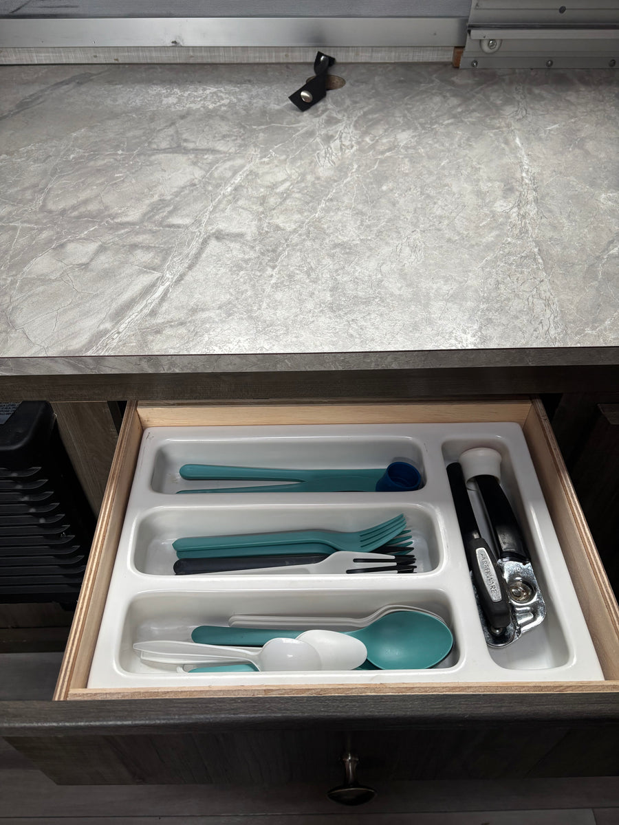 Open RV rental kitchen drawer featuring an organizer with teal, white, and black plastic cutlery and a can opener.