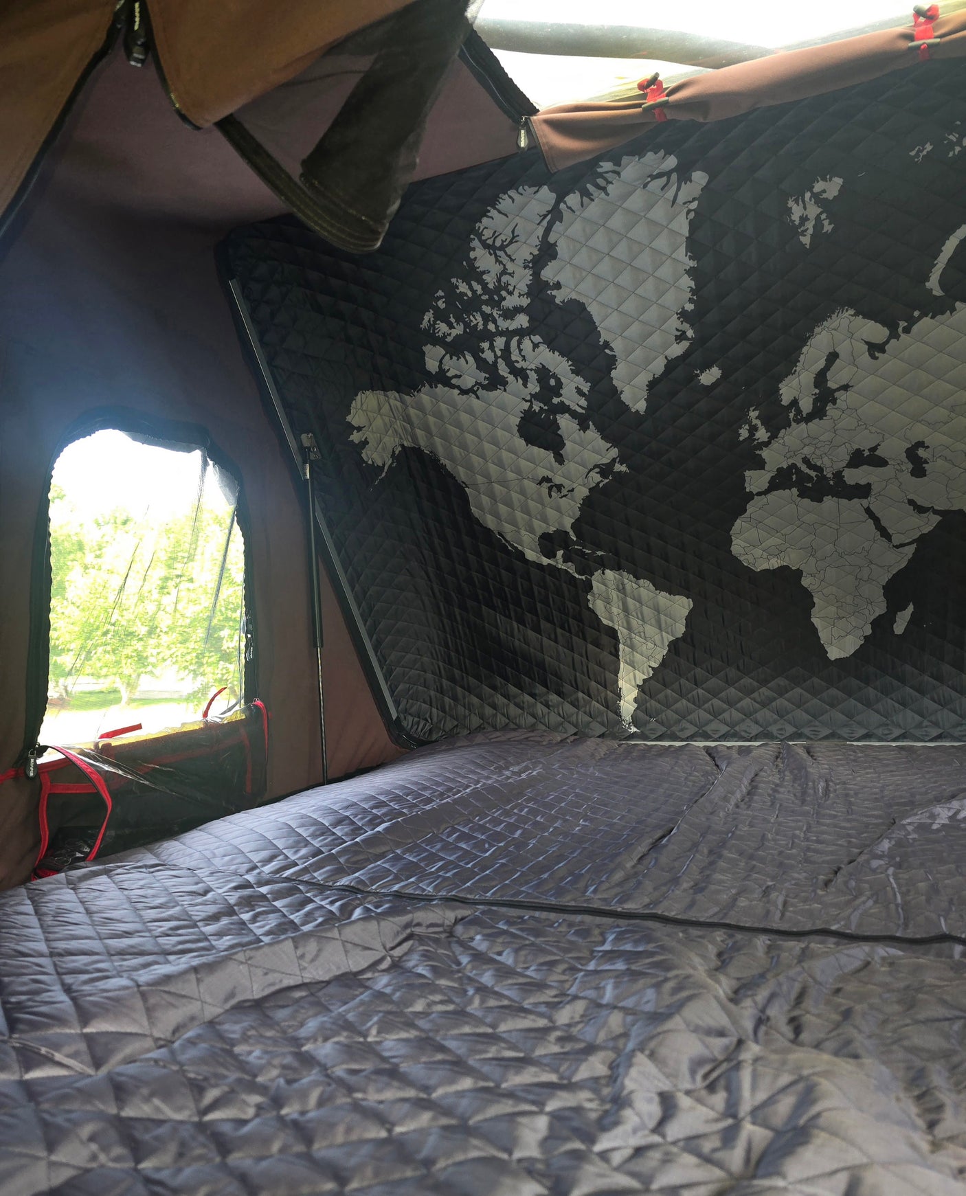 Explore in comfort with this RV rental interior: quilted bed, world map wall, and scenic window view.