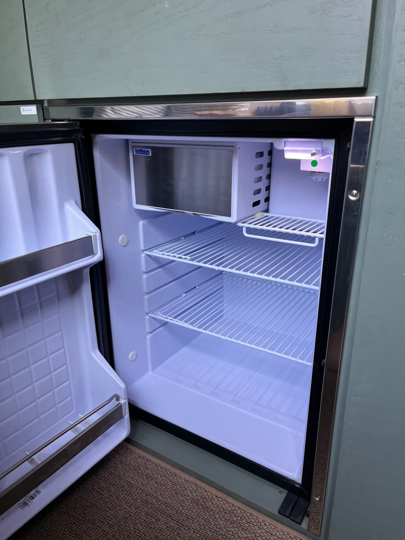 Bright interior of an open Isotherm compact refrigerator in an RV rental, showing wire shelves & freezer.