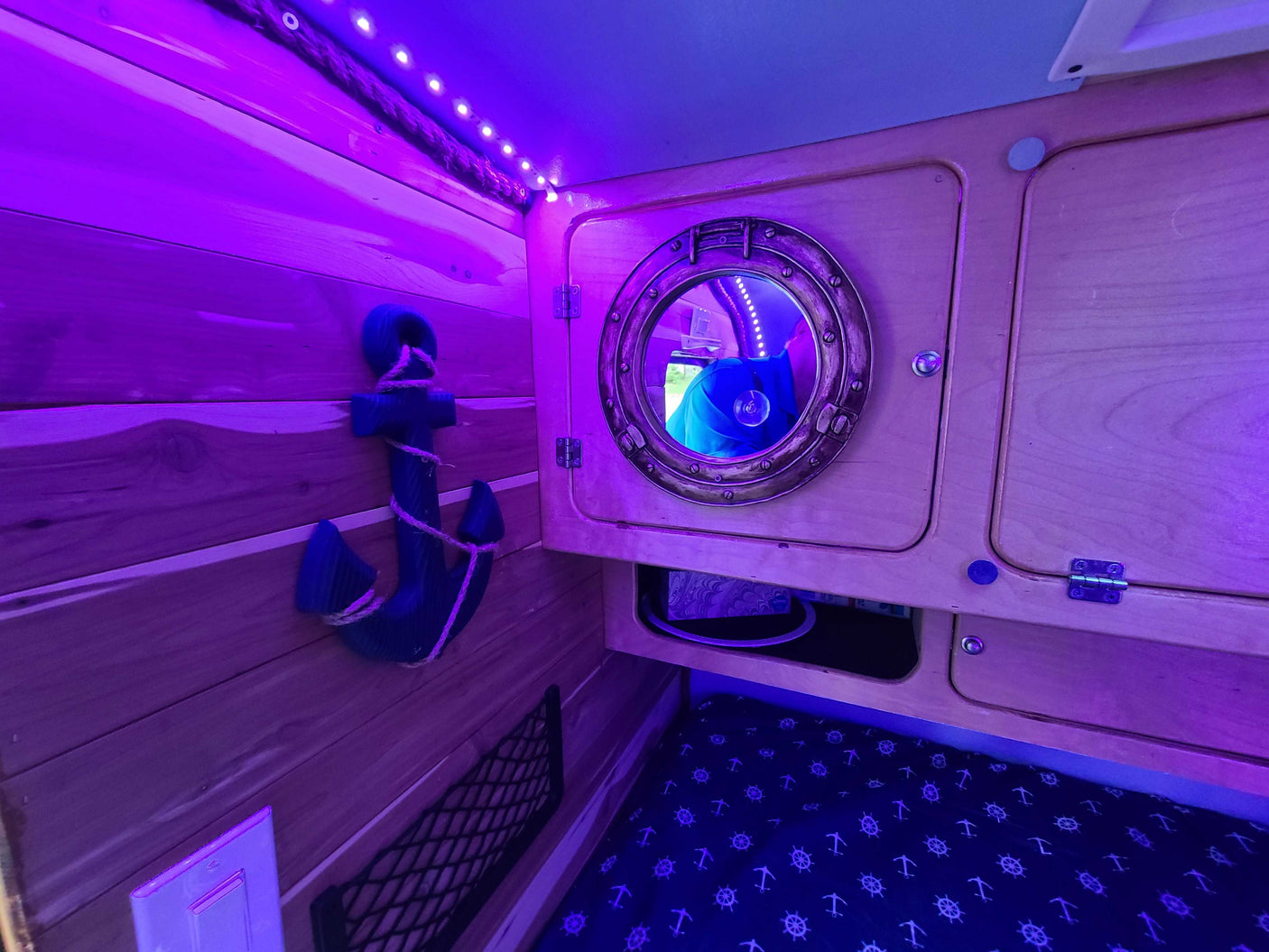 Cozy RV rental interior: purple-lit, nautical decor with porthole mirror, anchor, and patterned bunk bedding.