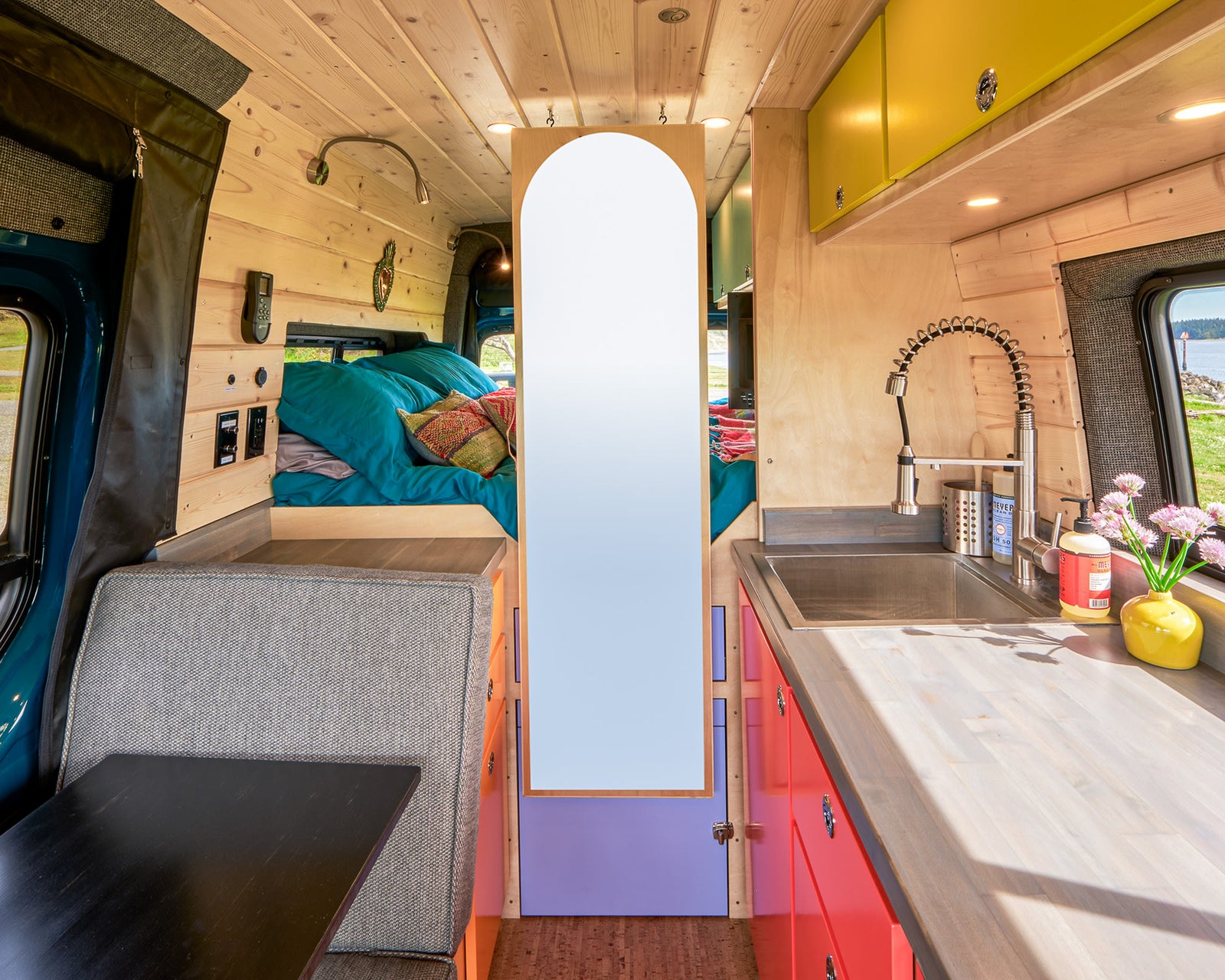 Spacious and modern RV rental interior, showcasing a compact kitchen, comfy bed, and versatile dining area in a wood-paneled camper van.