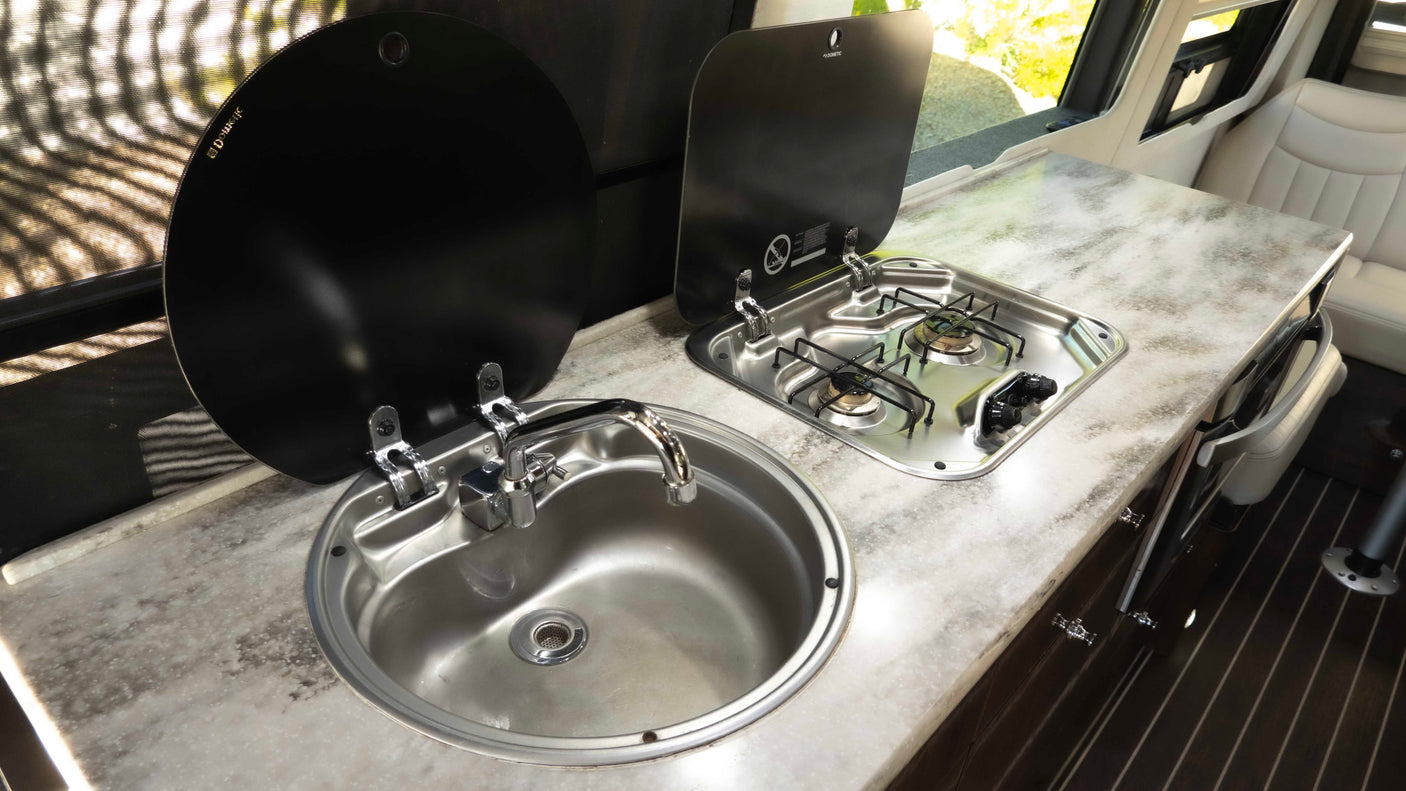 RV rental camper van kitchenette: chrome sink, two-burner stove with black covers, and patterned countertop for compact cooking.