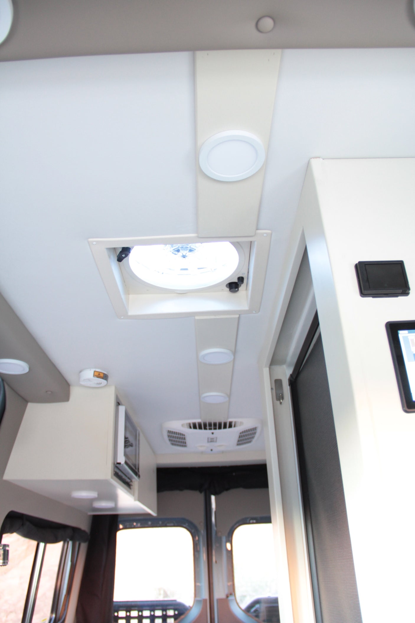 Bright RV rental interior, featuring ceiling lights, large vent, AC unit, and microwave. Ideal for comfortable travel.