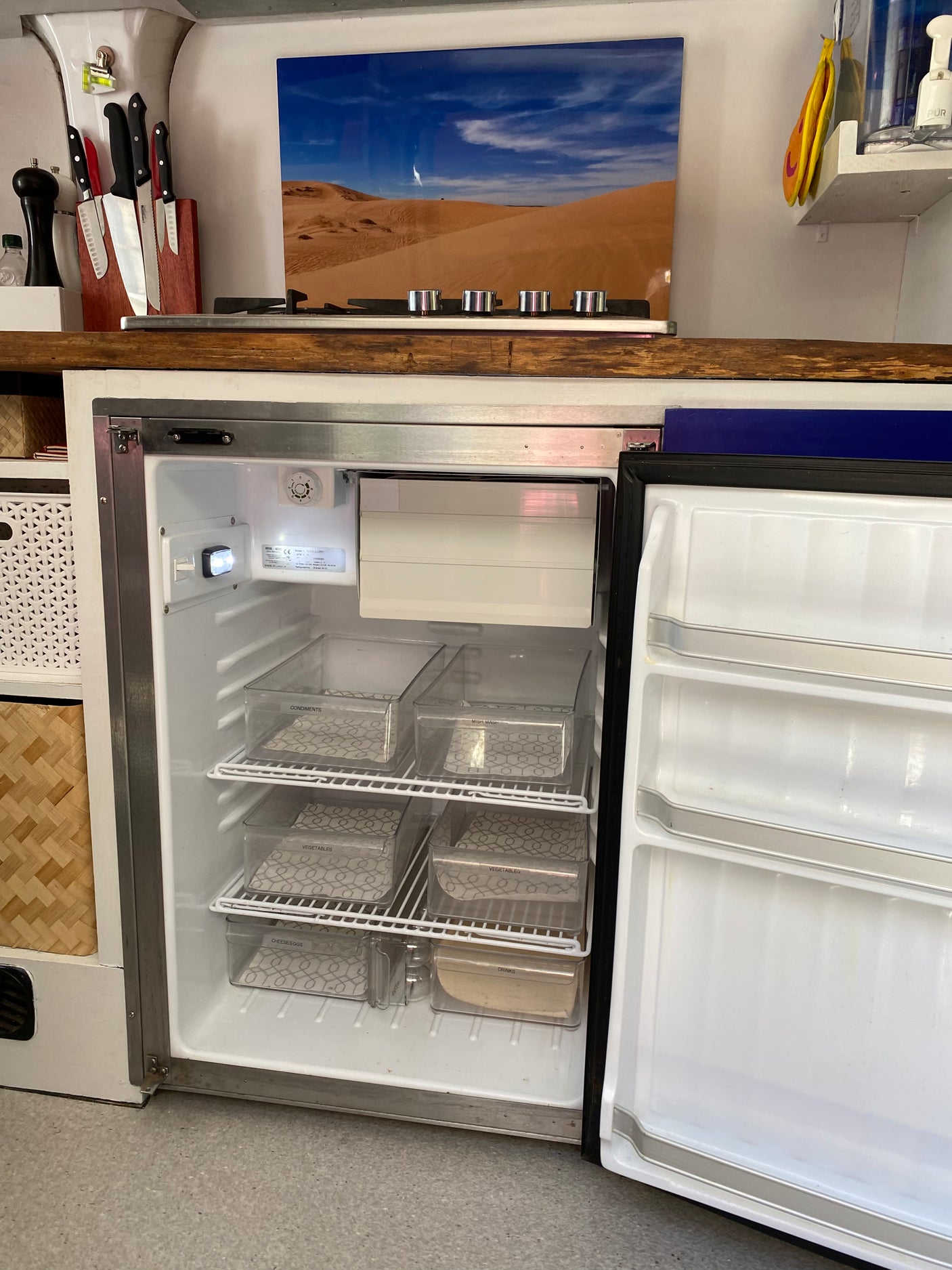 Inside an RV rental kitchen: a neatly organized fridge with labeled containers for condiments, veggies, and more, ideal for travel.