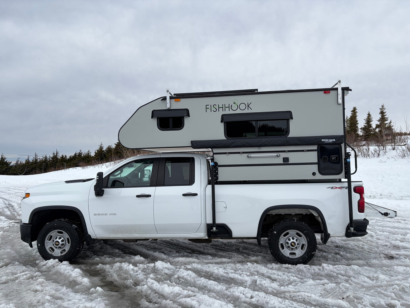 ready for an rv rental winter adventure in the snow.|White Chevrolet 2500 HD pickup with a 'FISHHOOK' truck camper on snowy ground