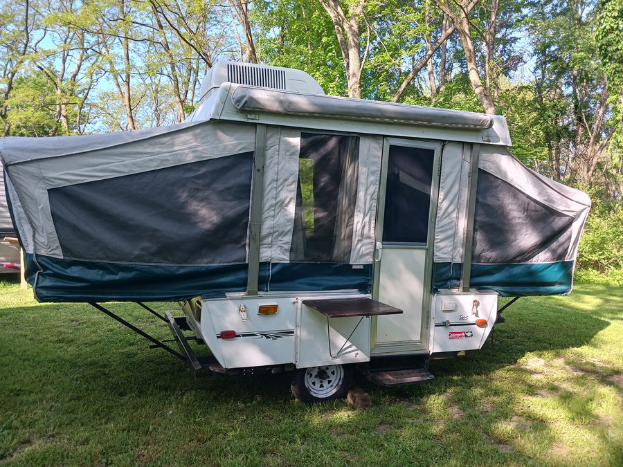 Explore nature with this Coleman pop-up camper. An ideal rv rental, it's set up outdoors with AC and a side table.