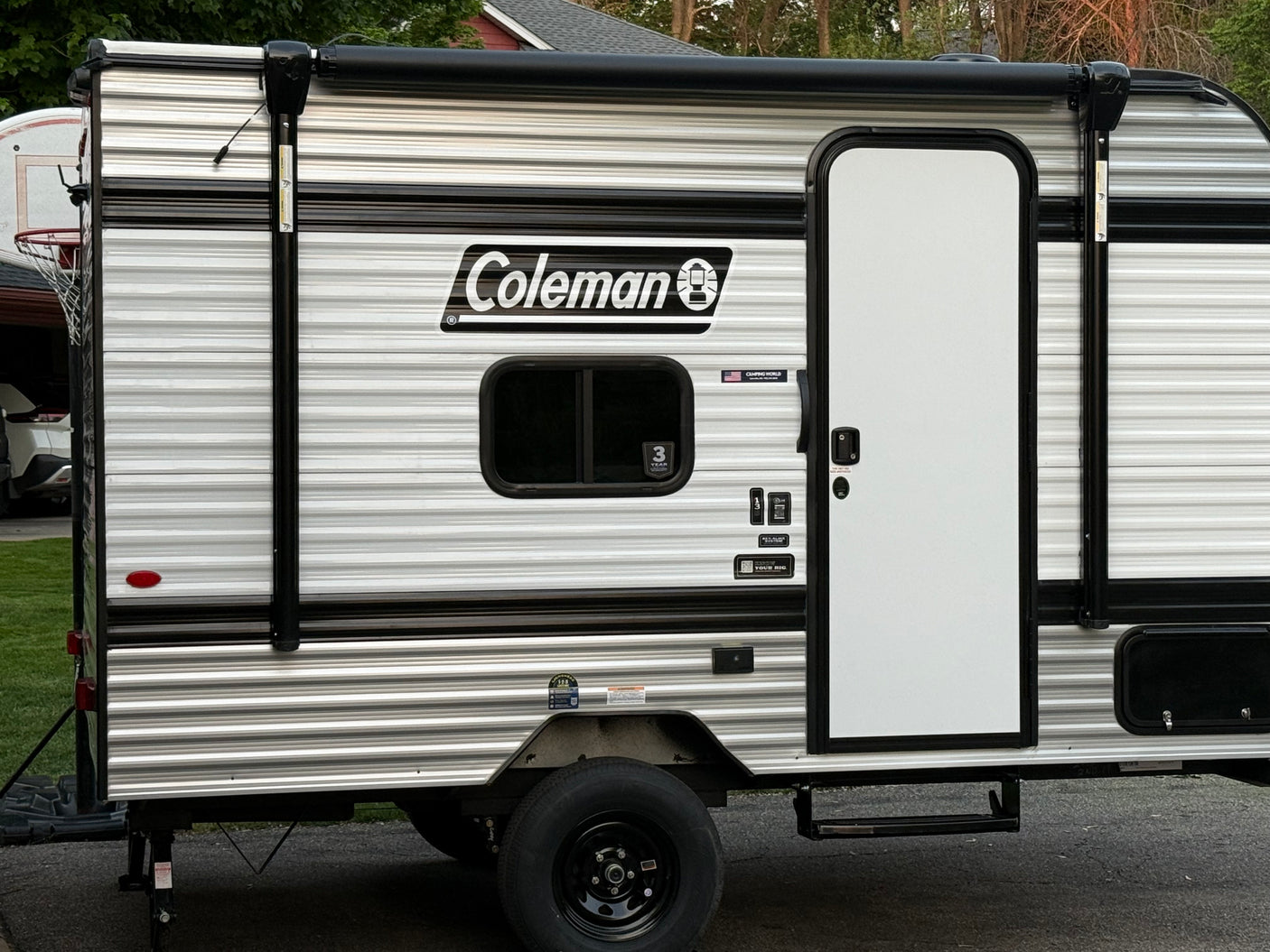 This Coleman RV rental, a striped travel trailer, features a side door, window, and retracted awning, ready for your next adventure.