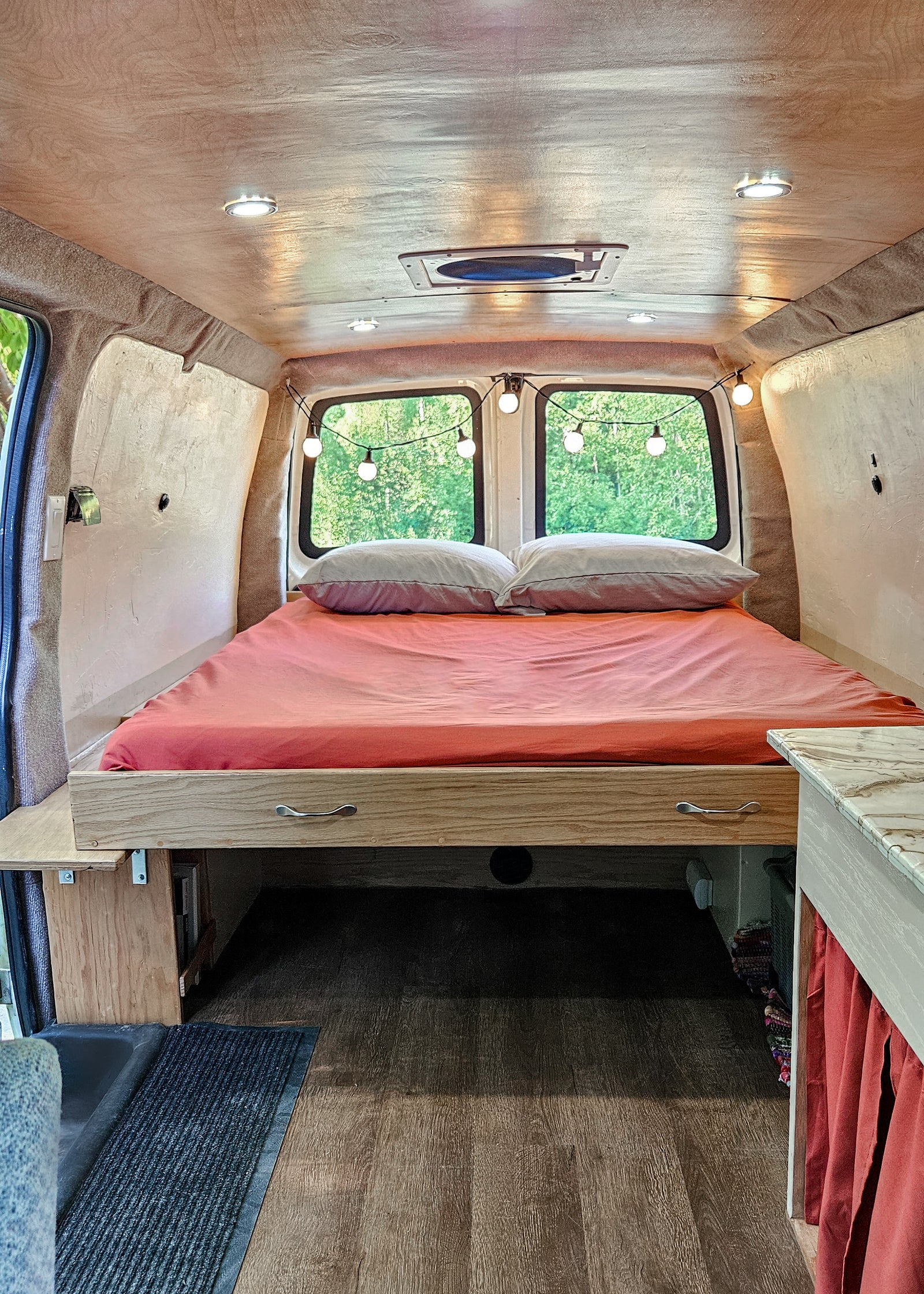 Cozy RV rental bed area featuring custom wood cabinetry, warm lighting, and a view of nature. Perfect for travel.