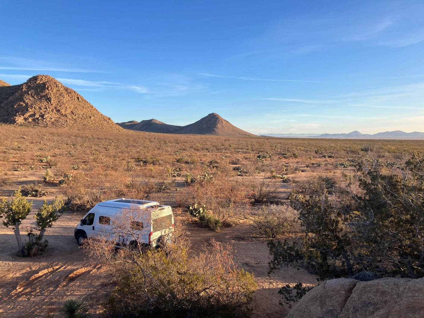 White RV rental van camping in a desert landscape with mountains and a bright blue sky.