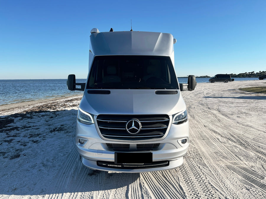 Front view: A silver Airstream camper van (rv rental) on a sunny sandy beach by the water. Ready for outdoor travel.