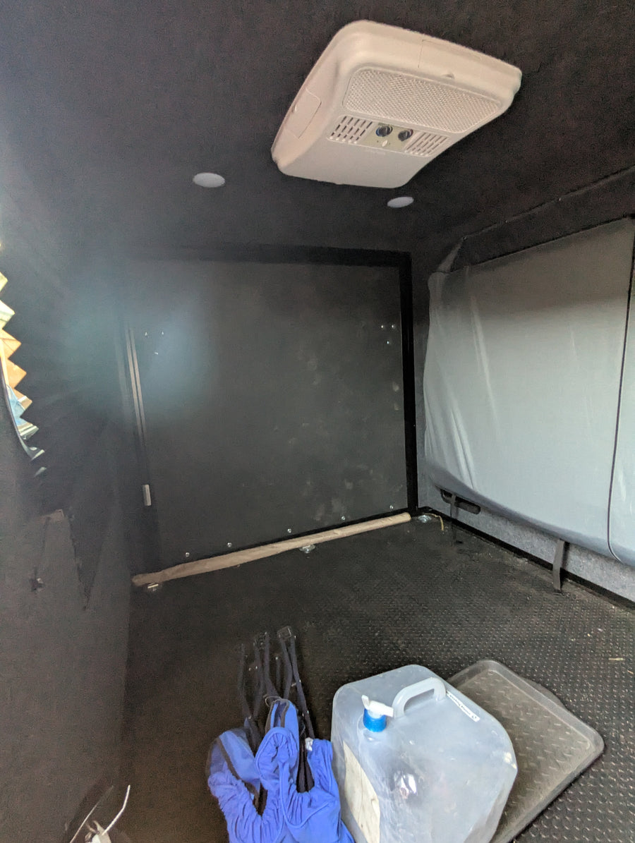 Compact RV rental interior with AC unit, storage, and water jug. Ideal for mobile living and travel.