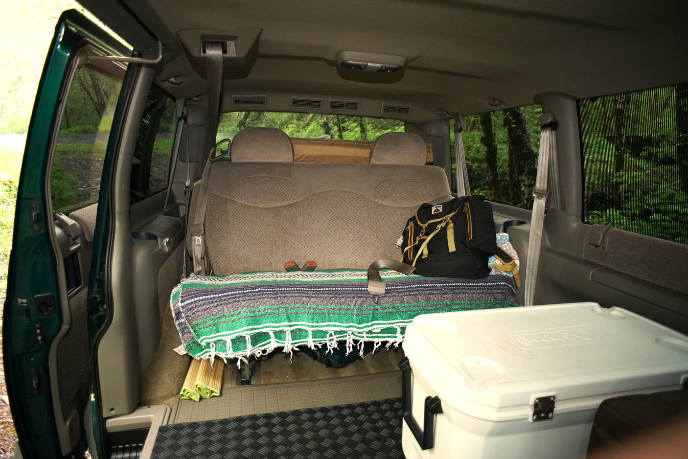 Inside an RV rental: a comfortable van interior with a bed-like seat, cooler, and outdoor gear.