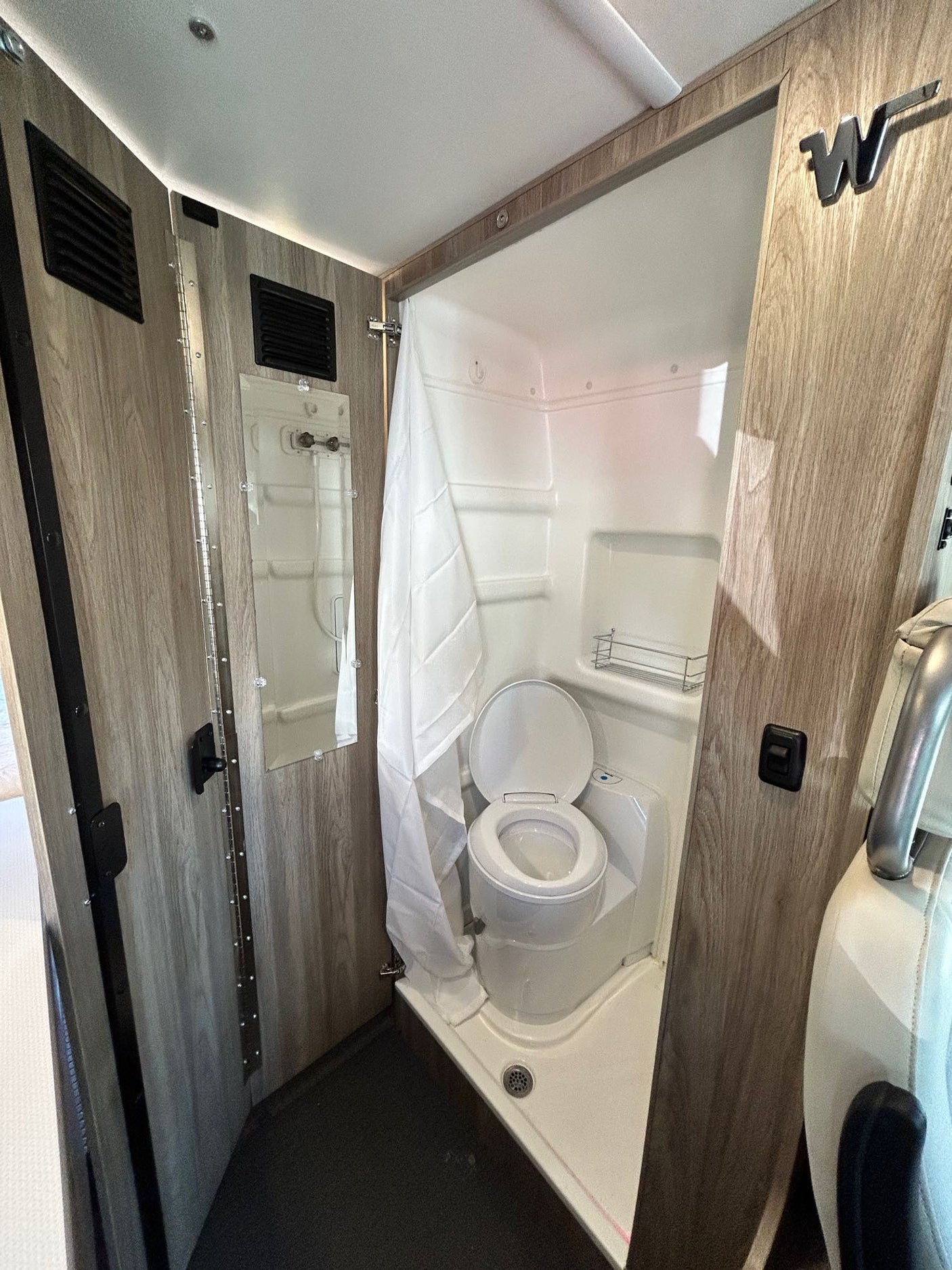 RV rental's compact wet bath: a white toilet inside a shower pan, with a shower curtain and wood-grain walls.