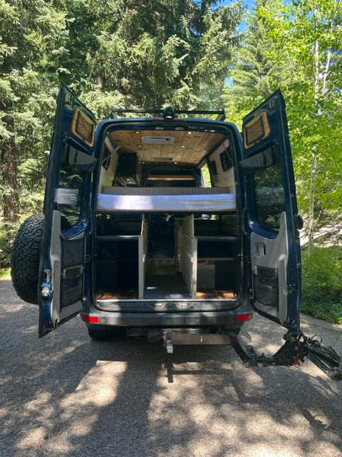 Ready for adventure! This customized RV rental features a warm wood interior, ample storage, and open doors in nature.