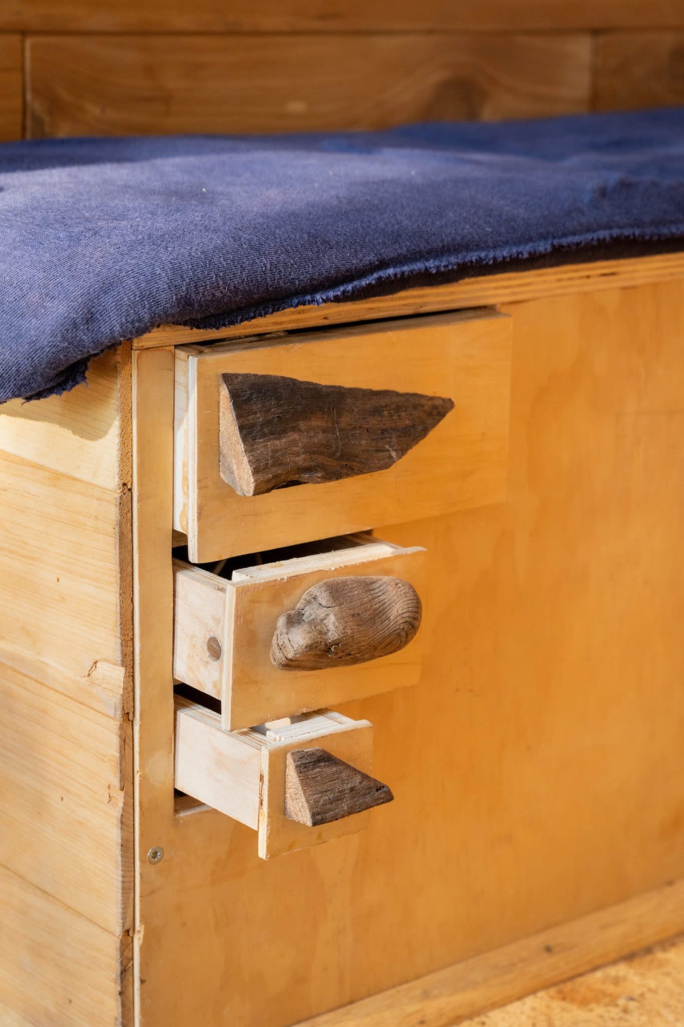RV rental comfort: Rustic wooden drawers with unique handles integrated into a bed frame, topped with a blue blanket.