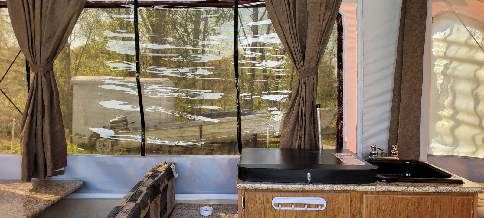 perfect for outdoor leisure.|An extended RV rental pop-up camper with mesh windows on a grassy campsite. A red generator sits nearby.|Cozy interior of an RV rental pop-up camper