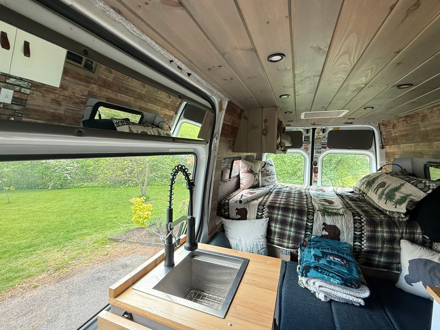 Cozy rv rental interior: custom wood-paneled camper van with kitchen sink, large window view, and comfy bed.