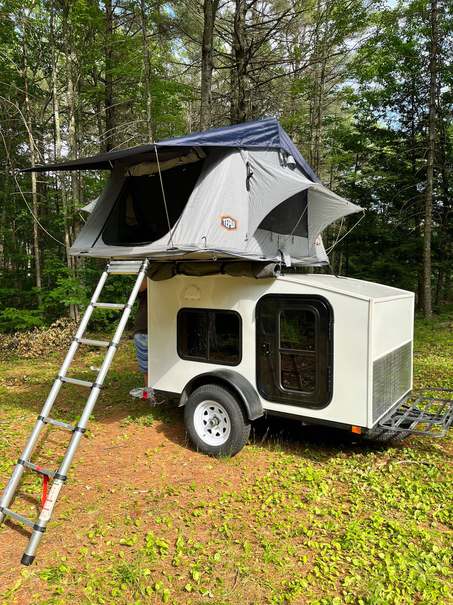 Compact RV rental: Teardrop trailer with a rooftop tent in a serene forest. Perfect for outdoor adventures and camping trips!|An RV rental camper trailer with a roof-top tent