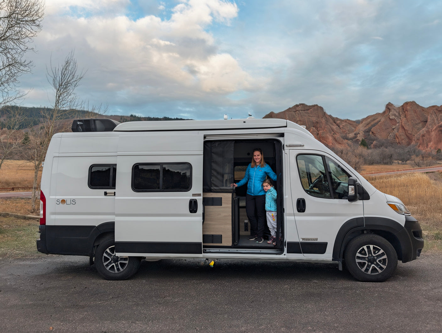 Woman & child in their white Solis RV rental van, parked near scenic red rock formations.