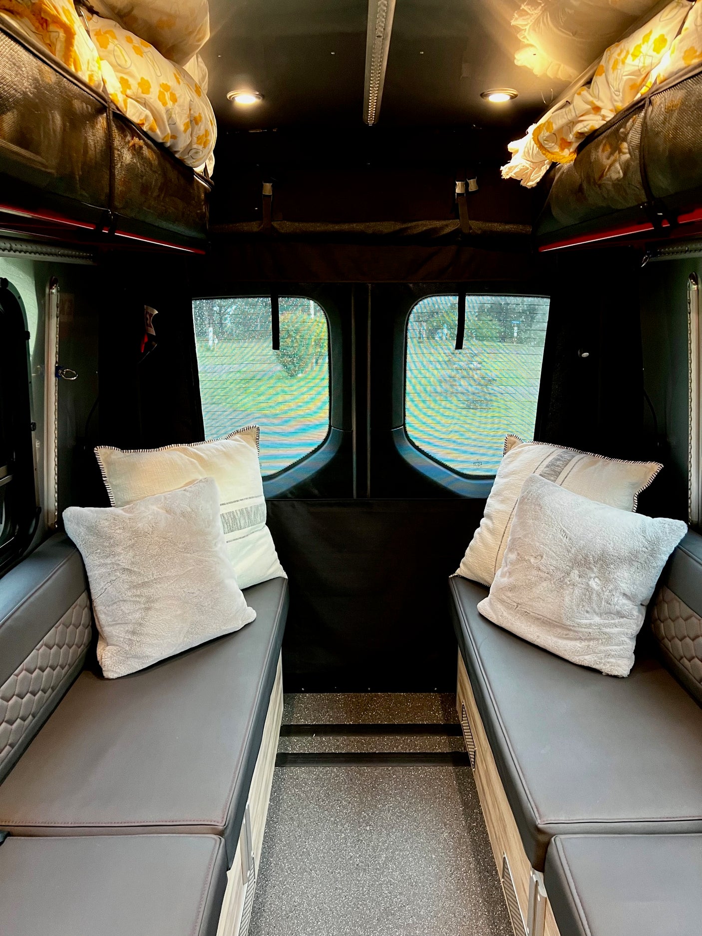 Inviting rv rental interior: dual benches with pillows, overhead storage, and screened windows for scenic views.