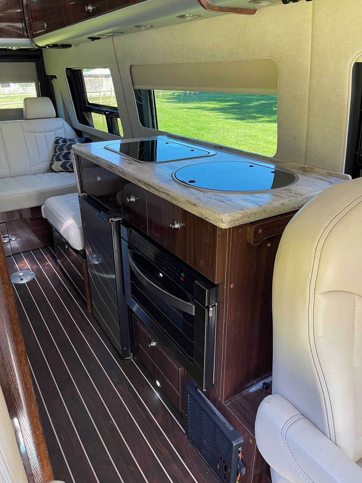 Luxury rv rental interior: Modern kitchenette with sleek cooktop, fridge, and oven, plus comfortable lounge seating. — photo 8