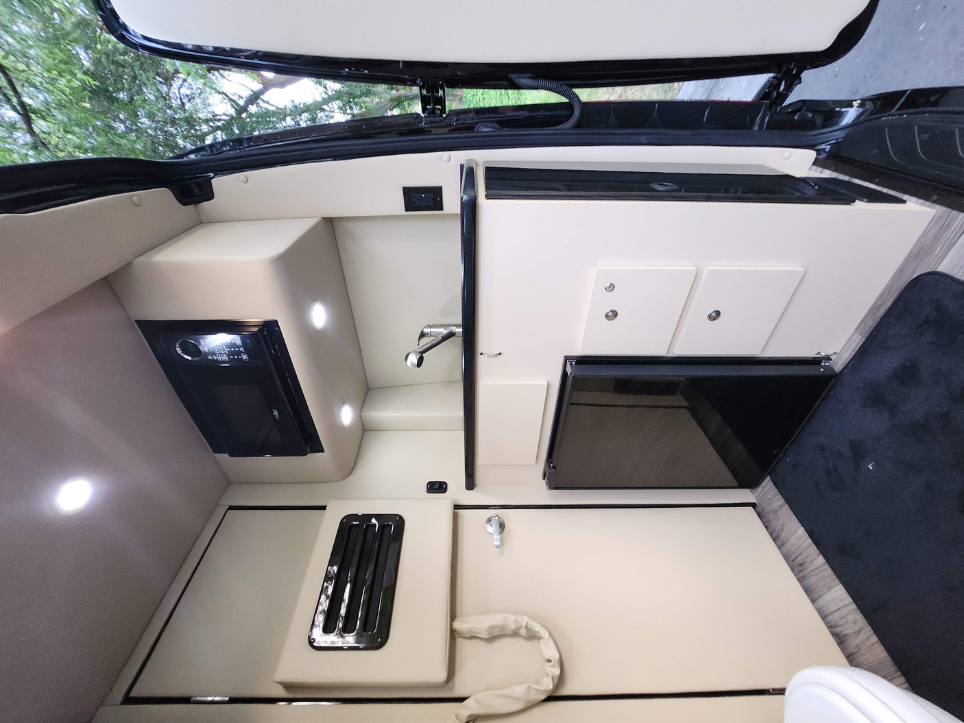 RV rental interior features a cream-toned kitchenette with microwave, sink, and mini-fridge, illuminated by recessed lighting.