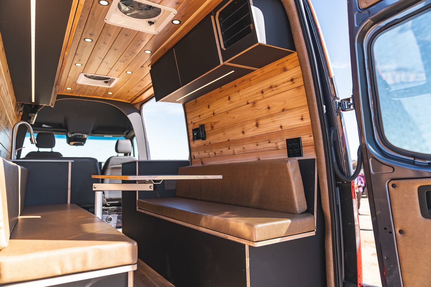 Inside an RV rental: wood-paneled interior with built-in seating, storage, and a movable table for comfortable travel.
