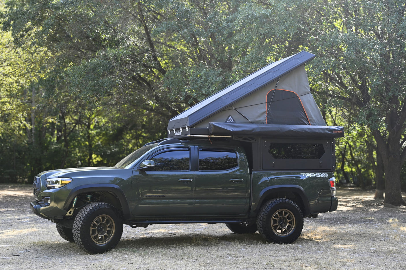 This rugged green Toyota Tacoma features a pop-up rooftop tent and bed camper, perfect for an RV rental wilderness trip.