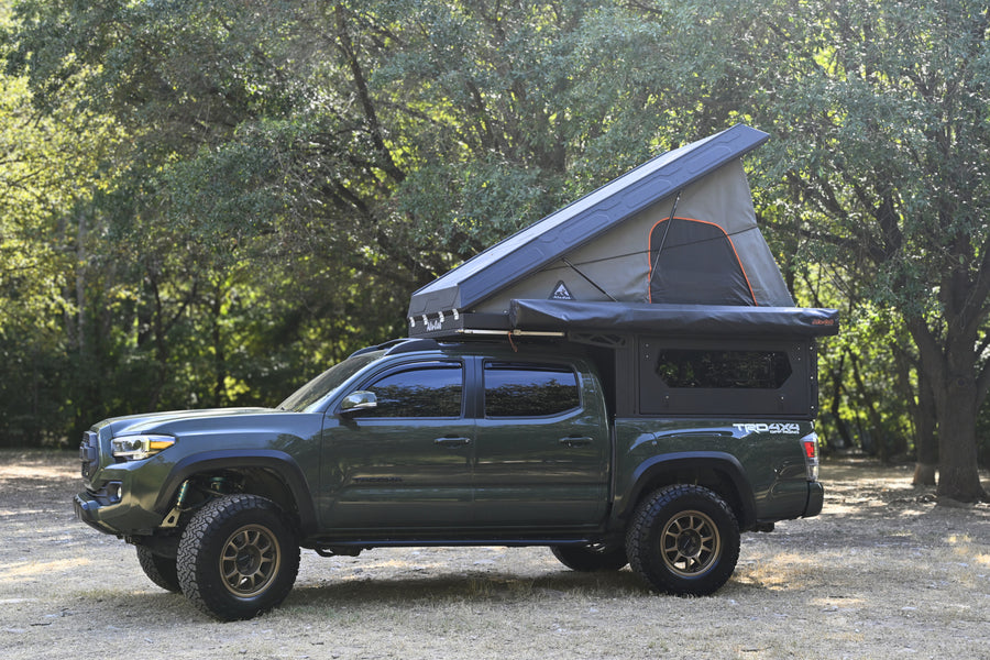 This rugged green Toyota Tacoma features a pop-up rooftop tent and bed camper, perfect for an RV rental wilderness trip.