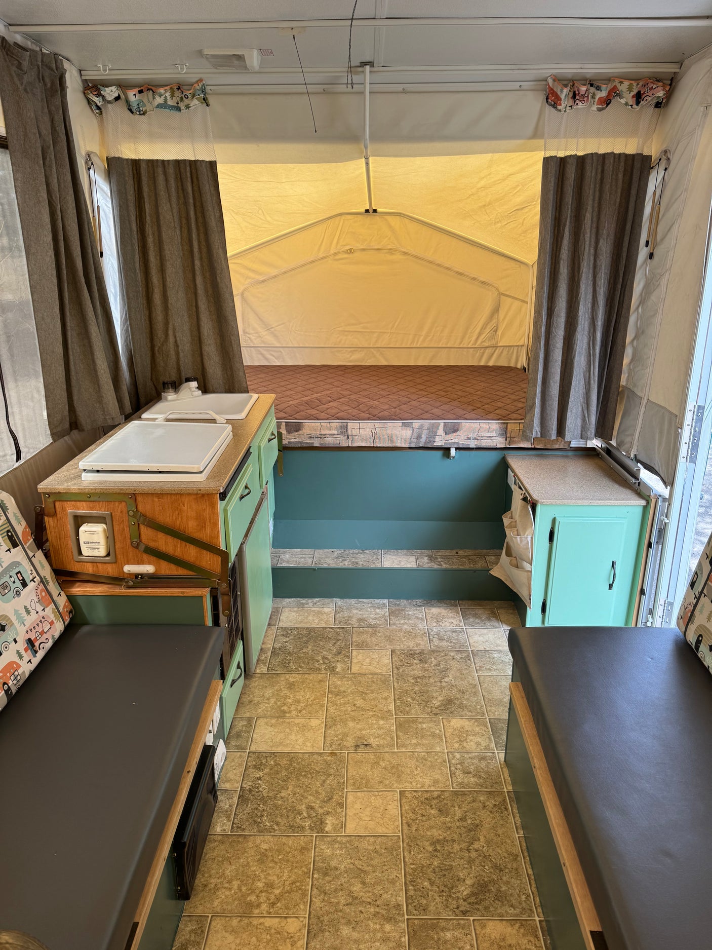 Step inside this inviting pop-up RV rental, featuring a cozy bed, compact kitchen, and versatile seating areas.