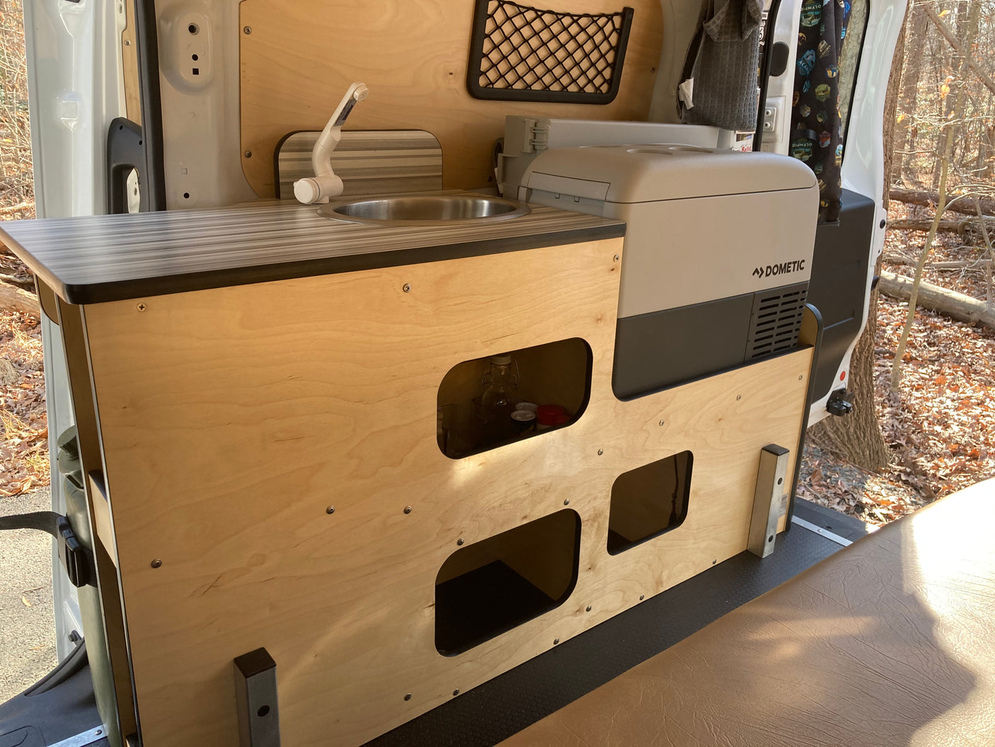 RV rental interior: practical wooden kitchen unit with sink, faucet, Dometic fridge, and open storage. Ideal for road trips.