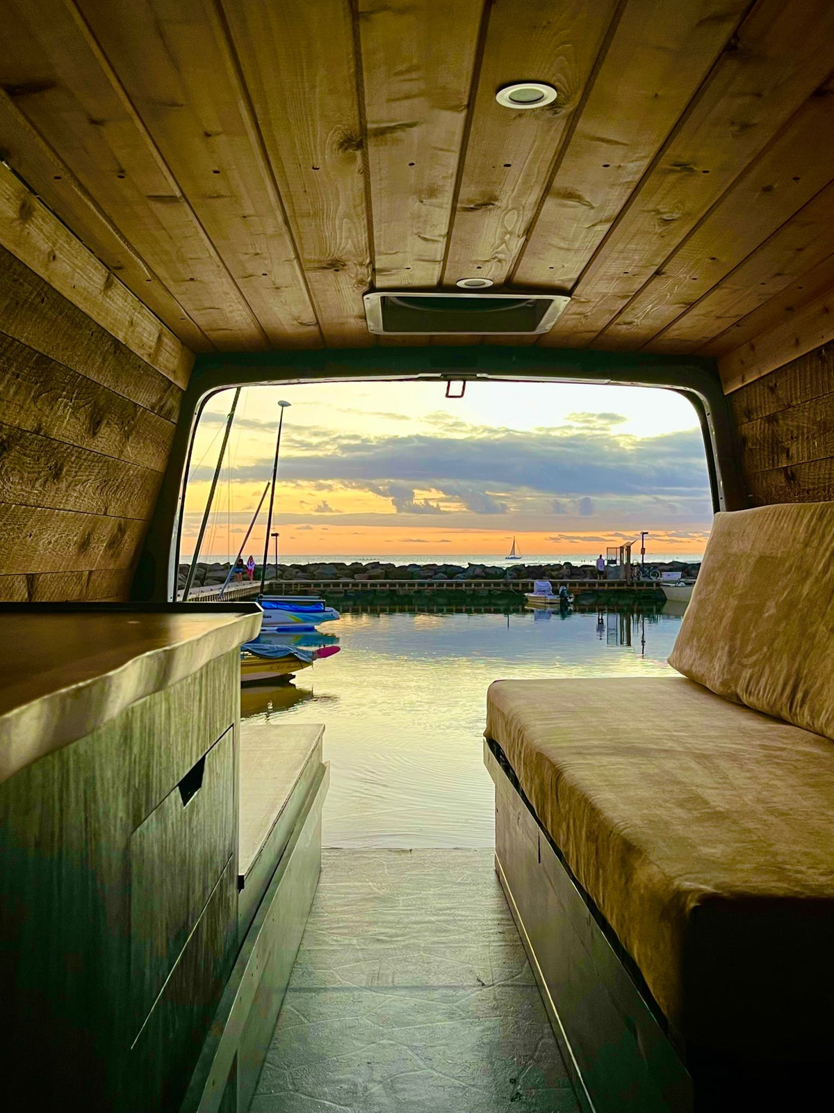 a bed with green bedding faces a harbor view with boats at a vibrant sunset.|Inside an **rv rental** — photo 2