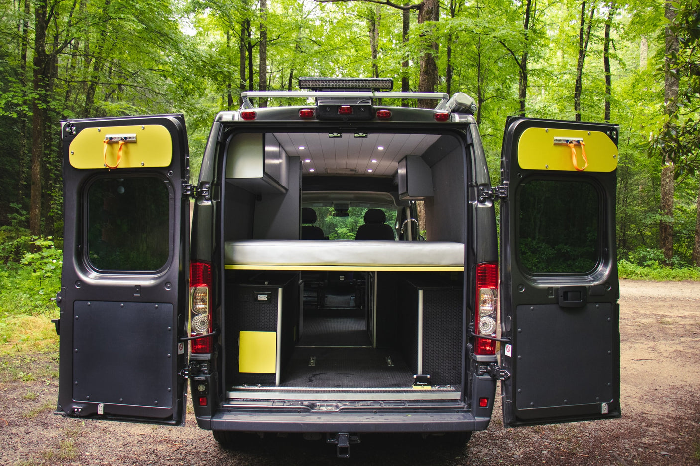 This RV rental camper van is open, revealing its customized interior with a bed & storage, ready for forest adventures.