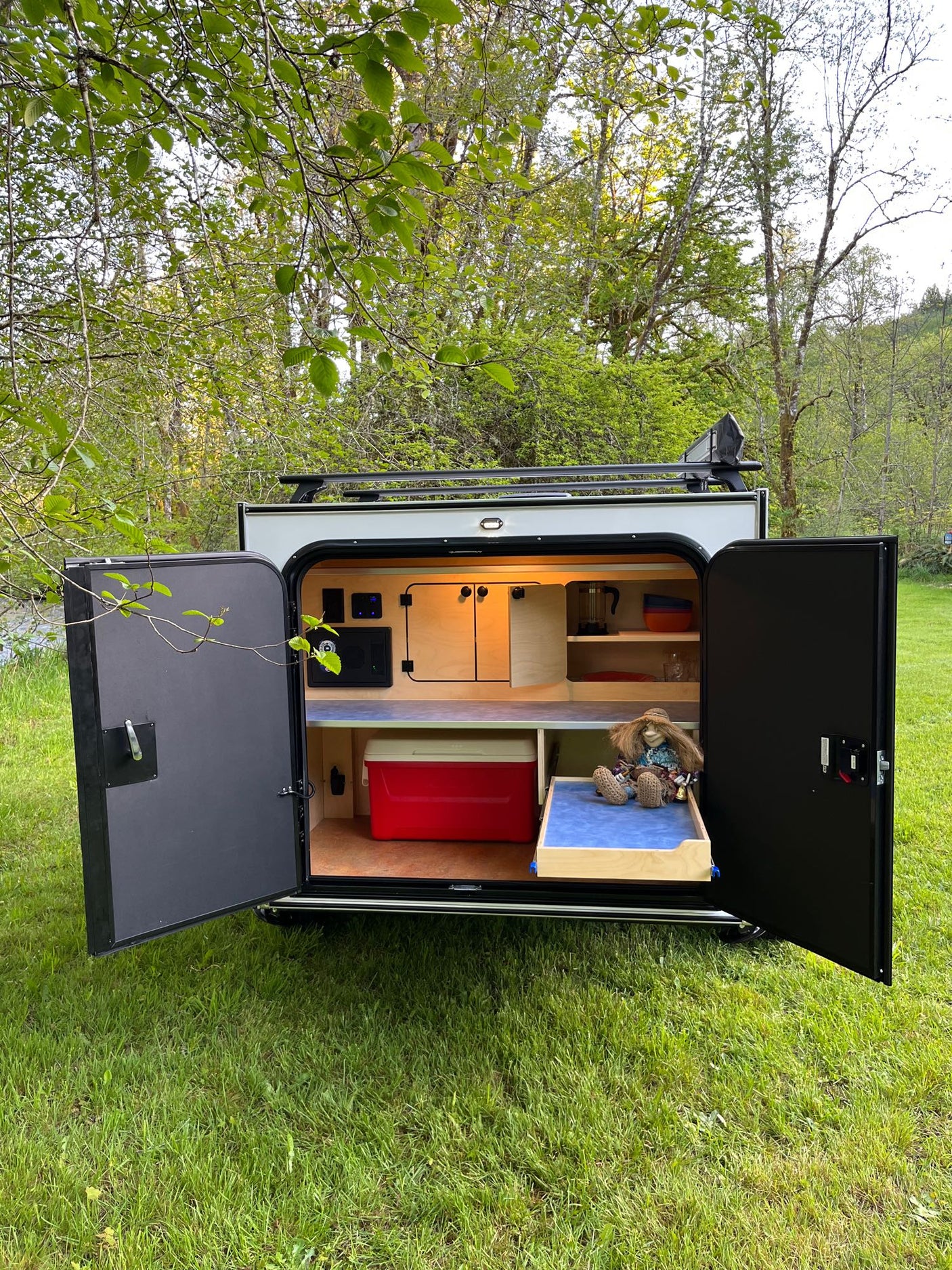 resting on a blue shelf.|Orange teardrop RV rental in nature with open door revealing cozy bed & forest view. Ready for adventure.|Vibrant orange teardrop camper