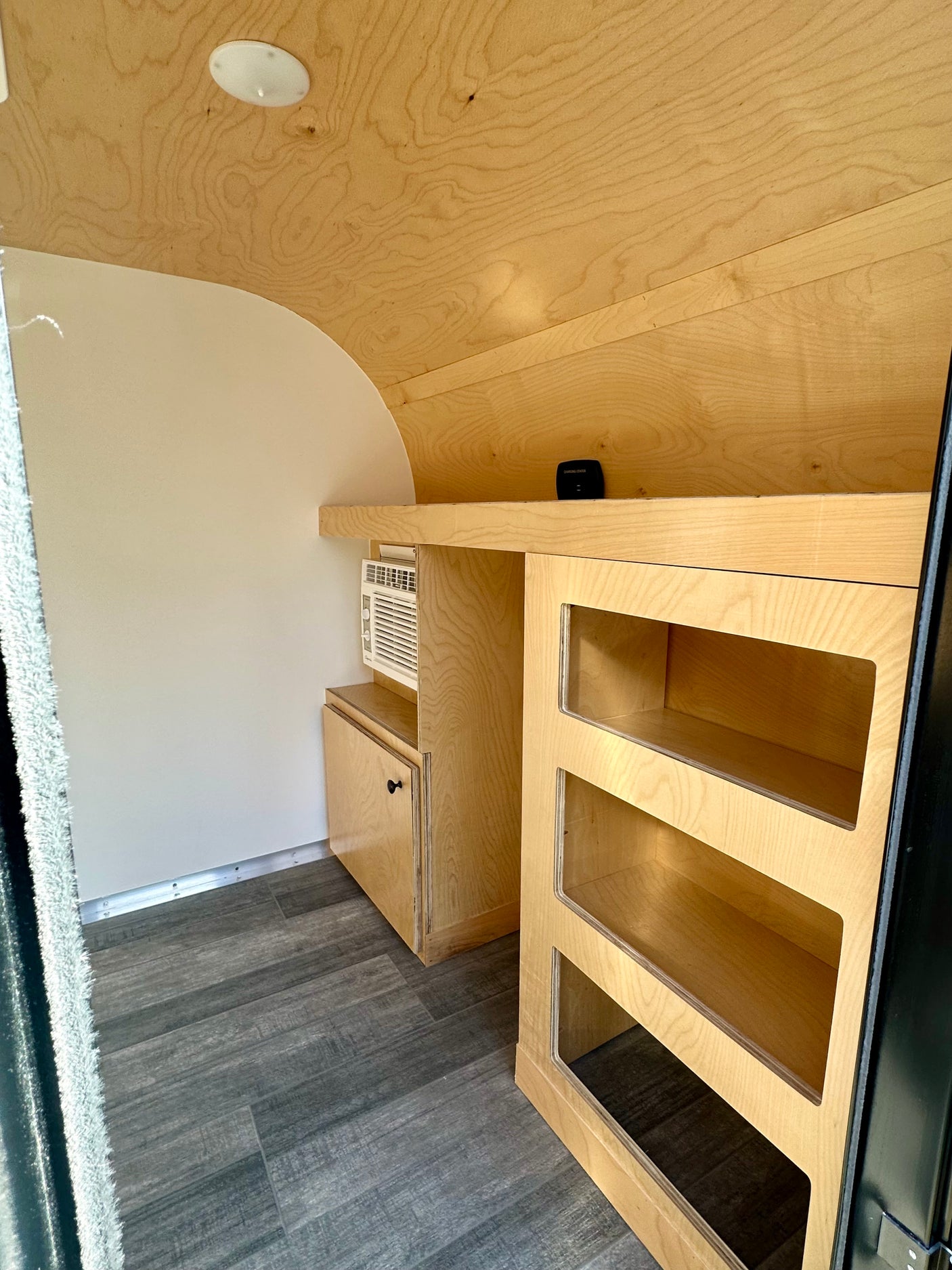Modern RV rental interior: light wood cabinetry, AC unit, and open shelves optimize space in this compact camper.