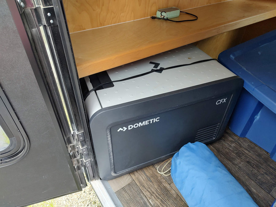 An RV rental interior shows a Dometic CFX portable fridge on wood-look flooring, with a blue tote and shelf.