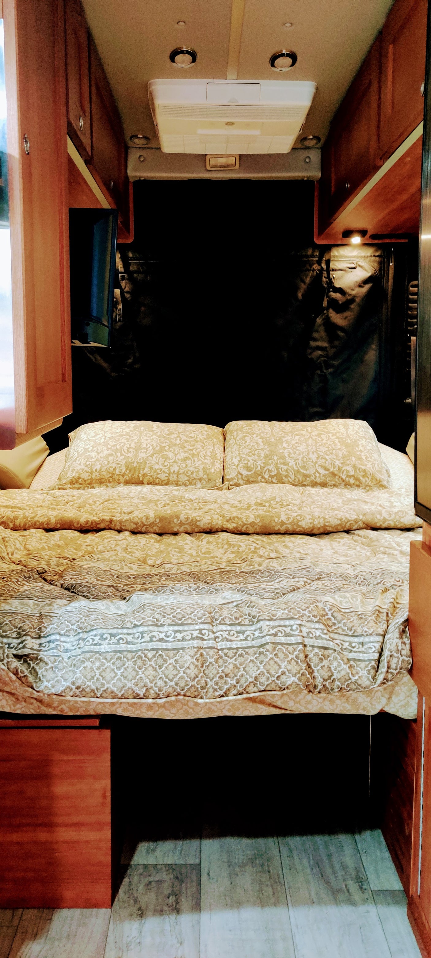 Relax in this RV rental's cozy bedroom. Features a patterned bedspread, AC unit, TV, and wood cabinetry.