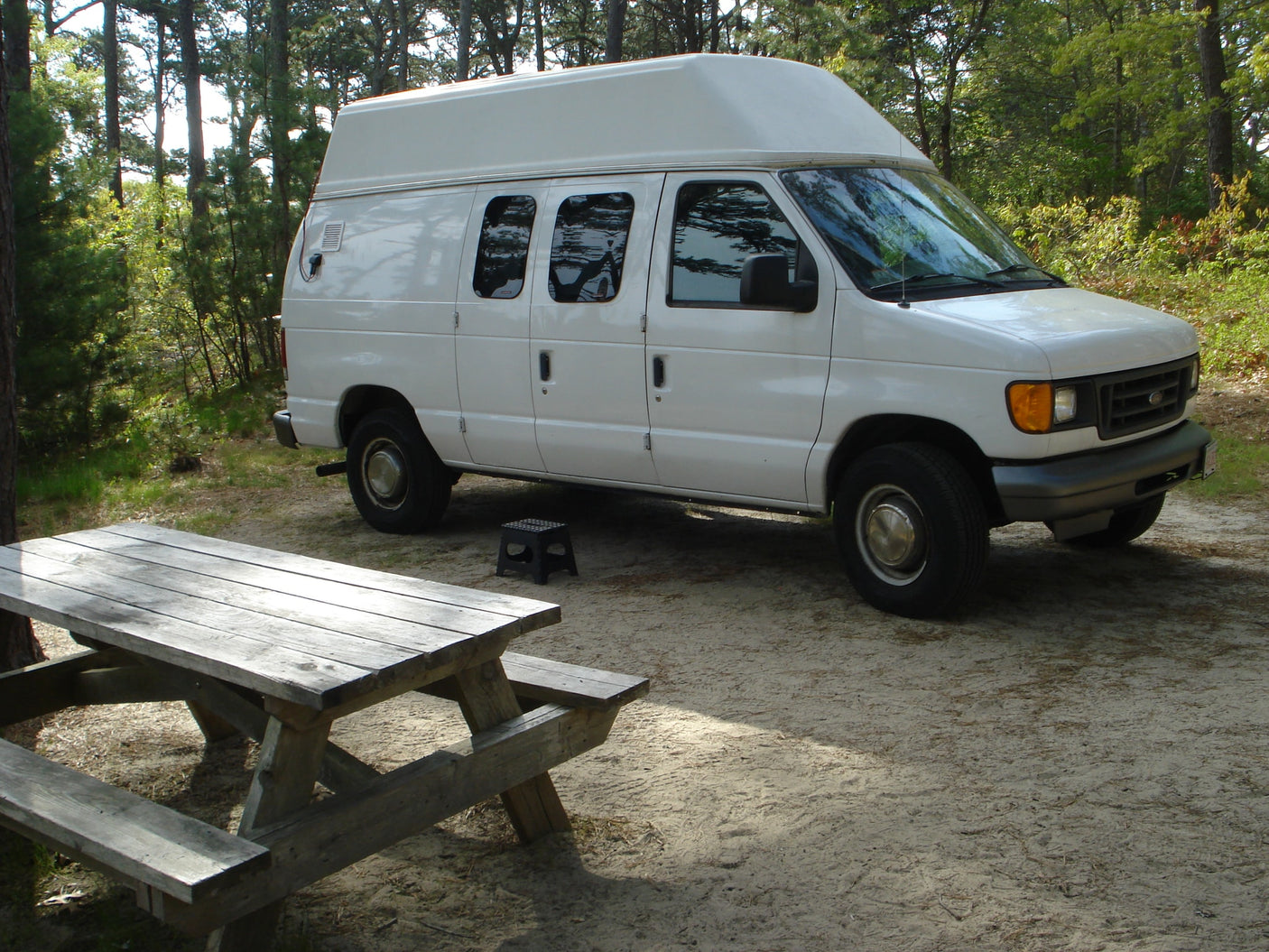 parked on gravel near fall foliage.|White Belaire RV rental parked amongst trees