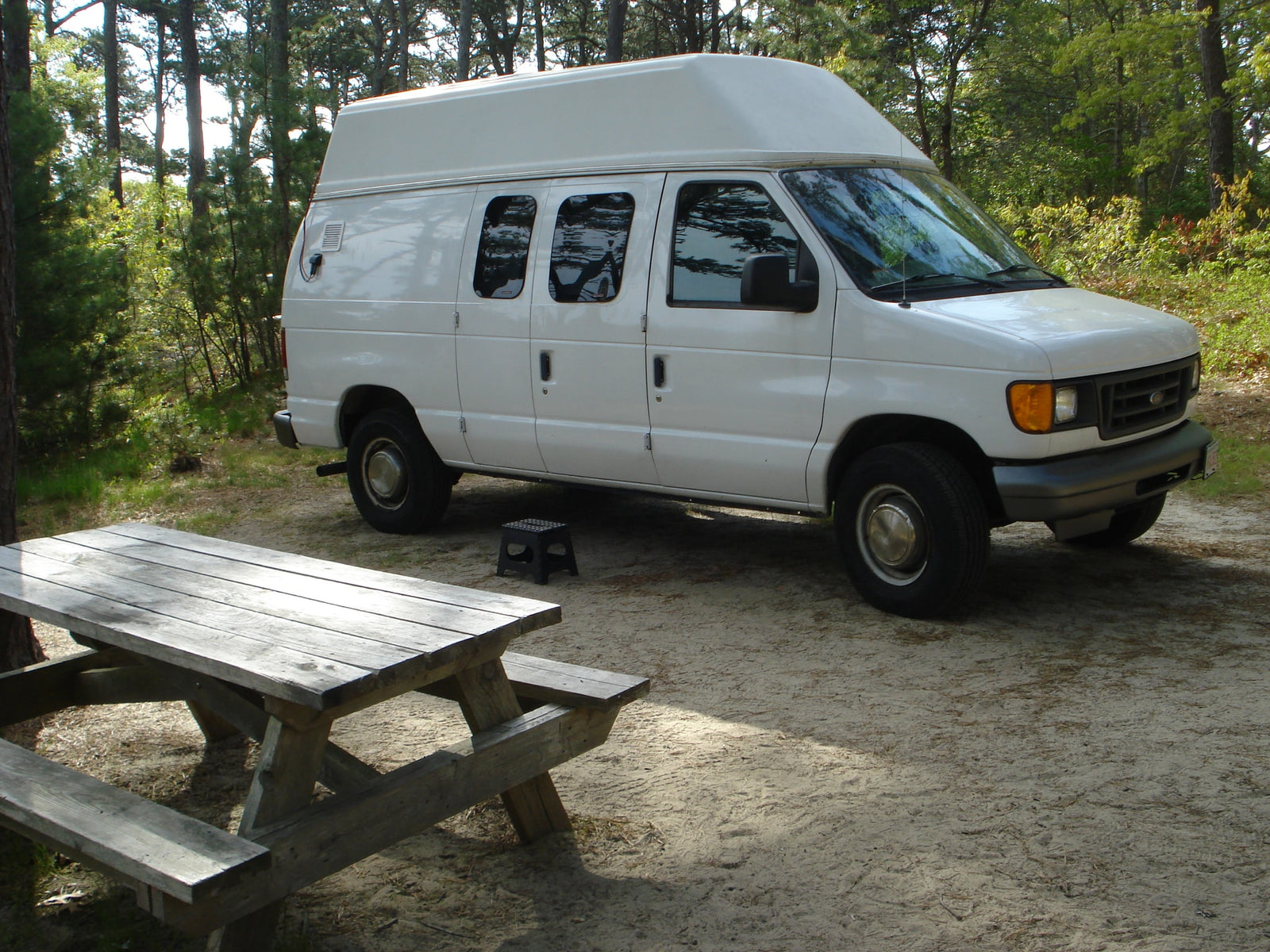 parked on gravel near fall foliage.|White Belaire RV rental parked amongst trees