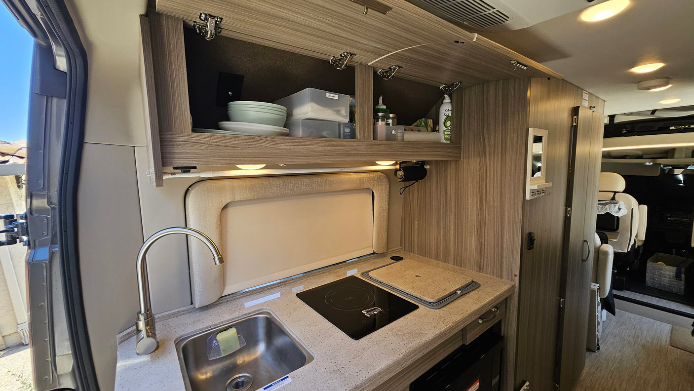 Inside an RV rental: a compact kitchen with a sleek sink, induction cooktop, and overhead storage for organized travel.