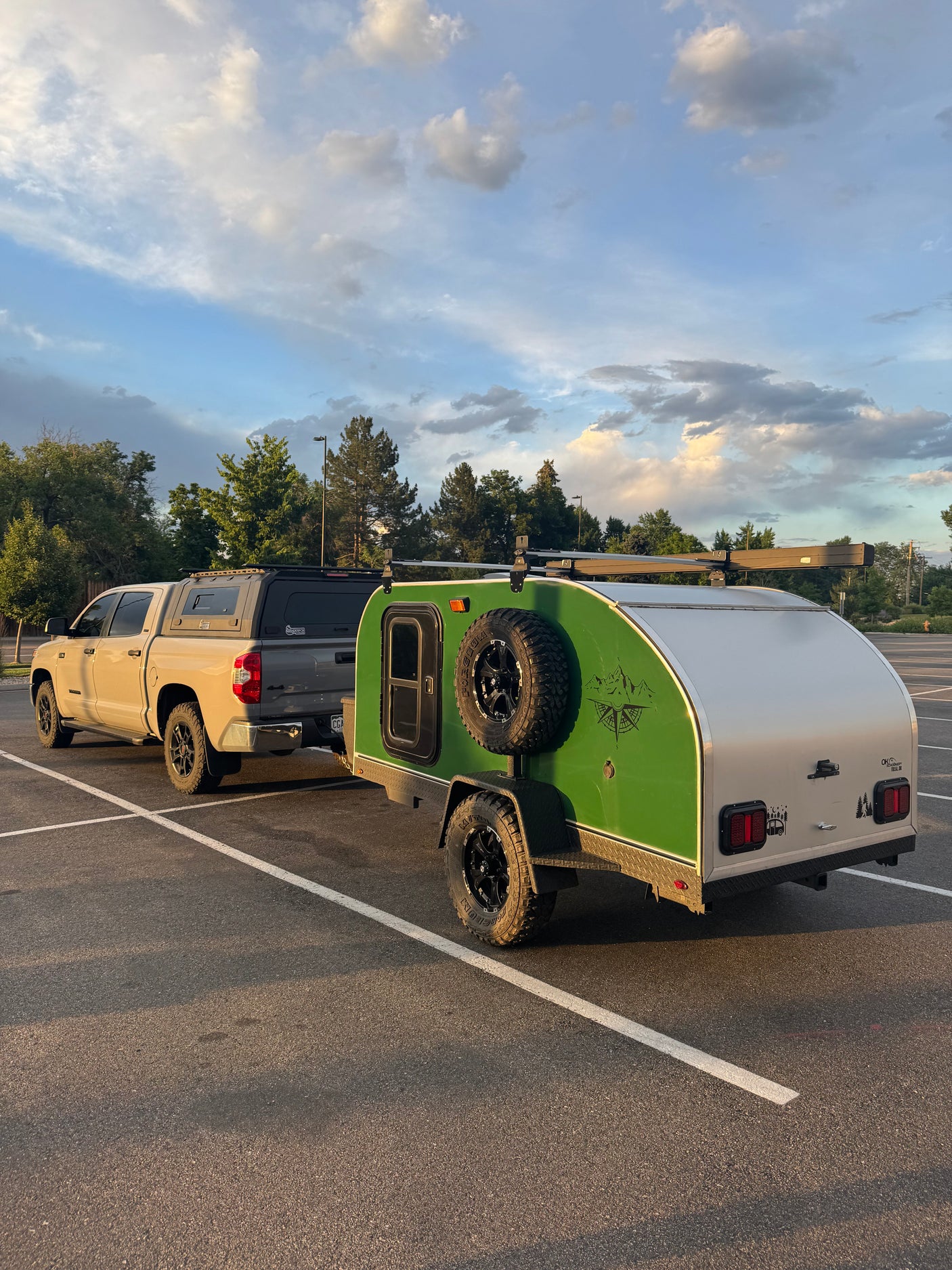 Adventure-ready RV rental: Tan pickup truck with camper shell towing a green teardrop trailer, perfect for camping adventures under a cloudy sky.
