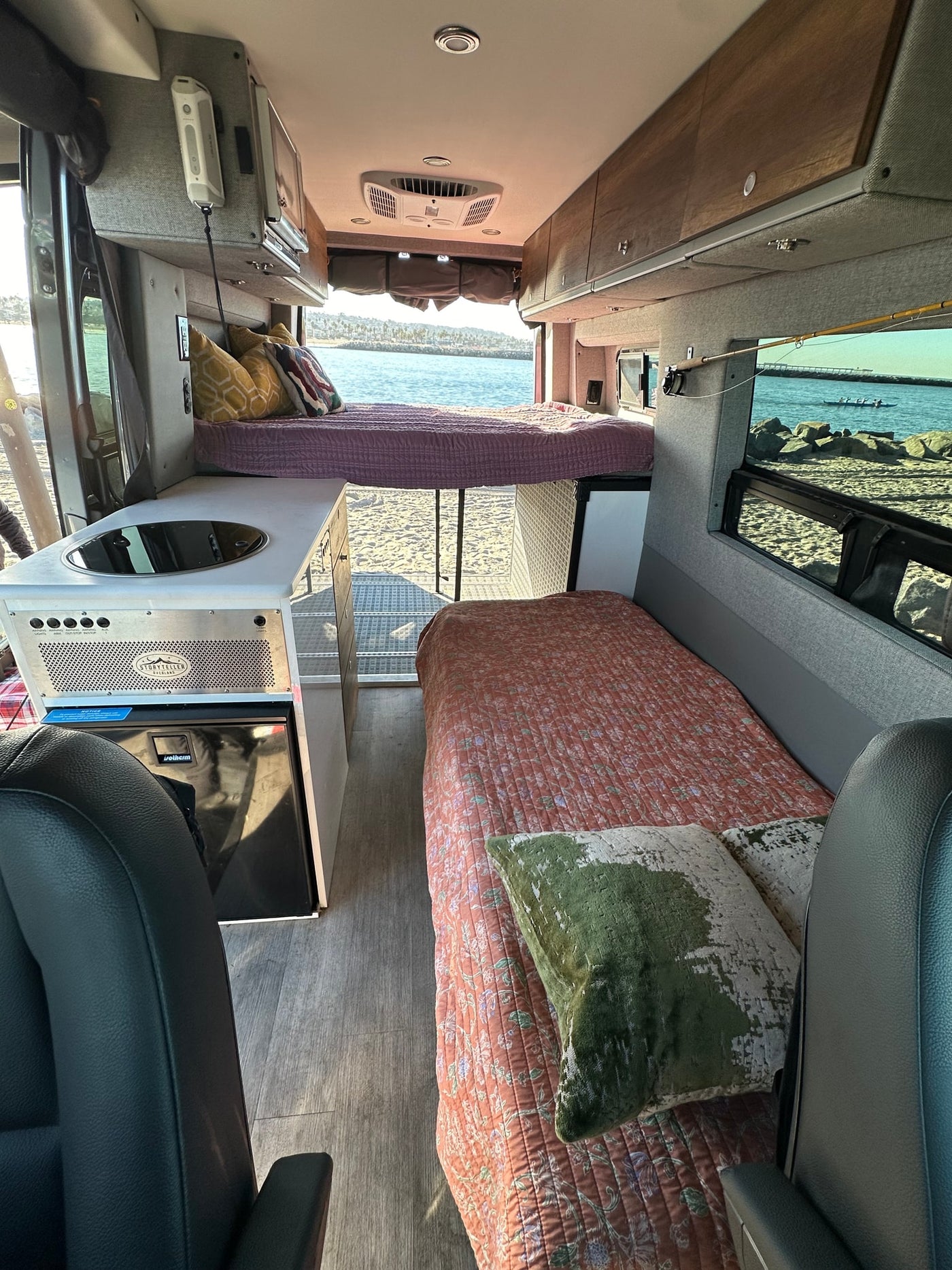 RV rental interior: two beds, kitchenette, and open rear door revealing a beach and ocean view. — photo 9