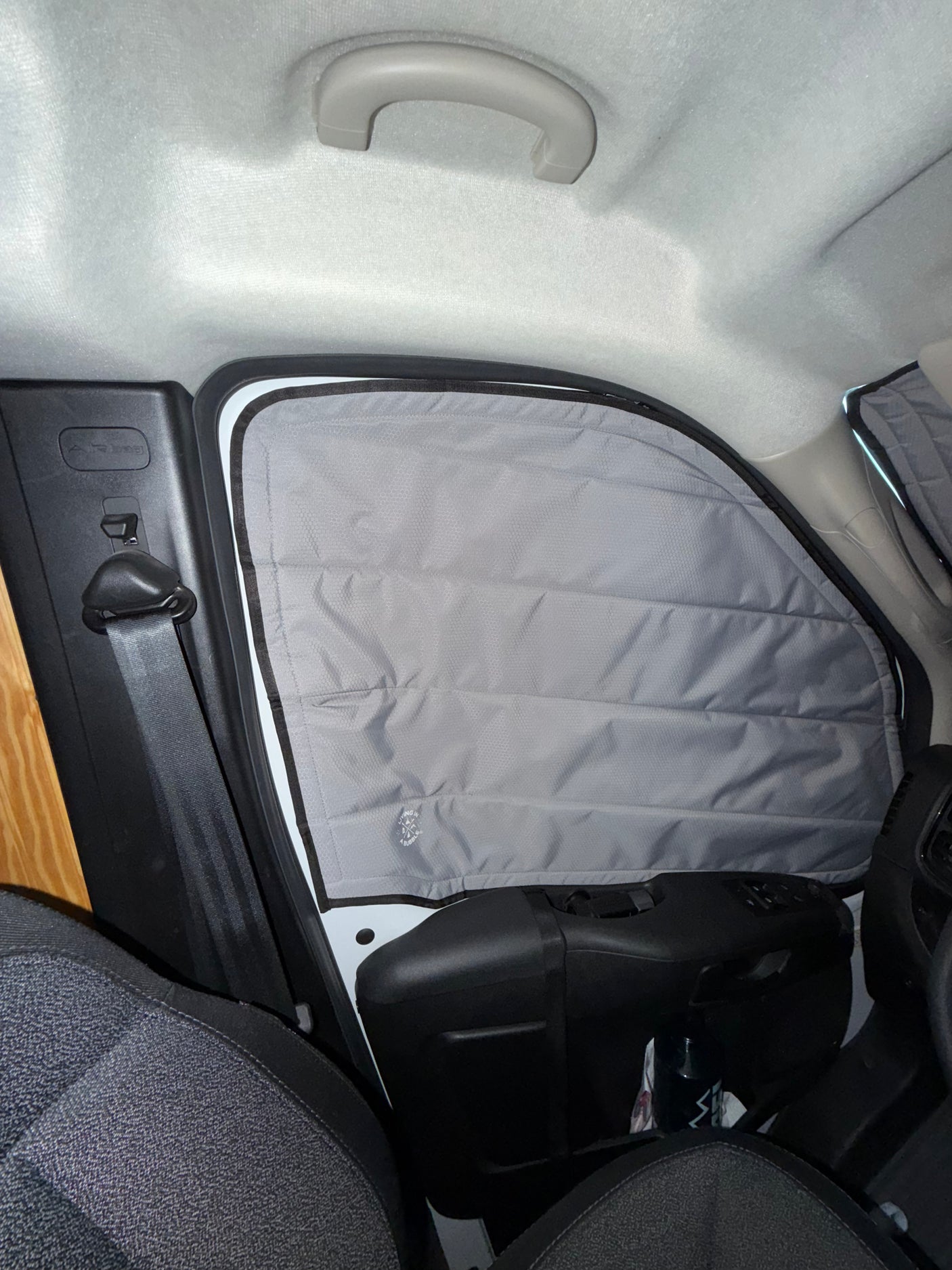 RV rental camper van interior showing a gray, insulated window privacy screen, a seatbelt, and car ceiling.