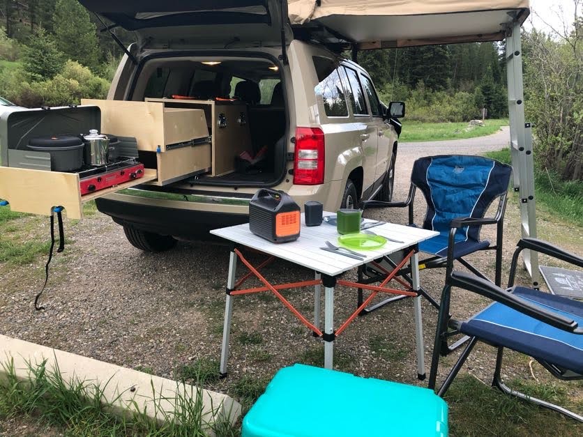 and full campsite furniture ready for adventure.|This RV rental alternative features a tan SUV with a deployed roof-top tent and ladder for wilderness camping.|Car camping setup with SUV-integrated kitchen and outdoor dining for your next adventure. Perfect alternative to an RV rental.|RV rental adventure! Enjoying a hot meal cooked outdoors on a portable camping stove. Perfect for road trips and nature.|SUV car camping setup: custom storage — photo 6