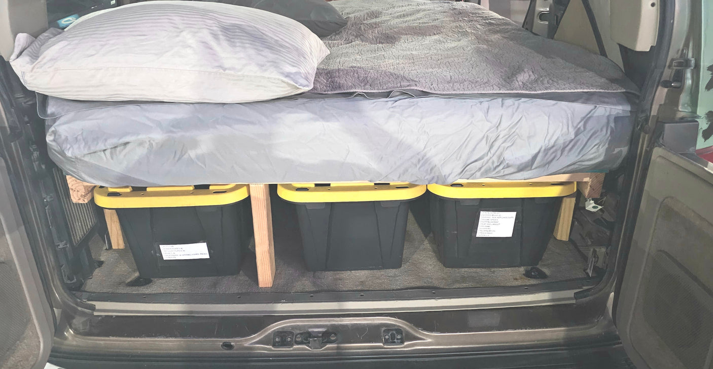 Efficient car camping setup in an RV rental with an elevated bed and labeled storage bins for gear.