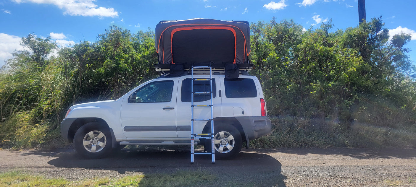 White Nissan Xterra with a deployed rooftop tent and ladder, an ideal RV rental for off-road camping.