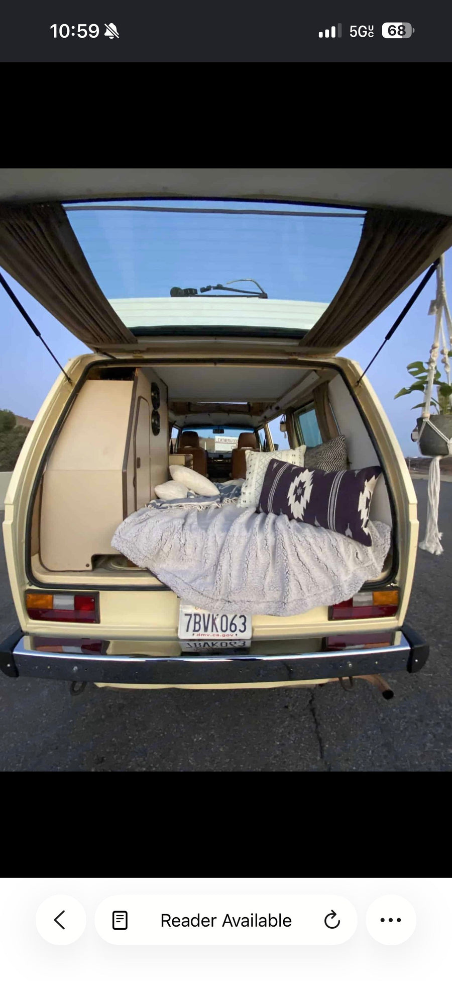 Inside a cozy vintage camper van RV rental, the open tailgate reveals a bed with patterned pillows, storage, and a hanging plant.