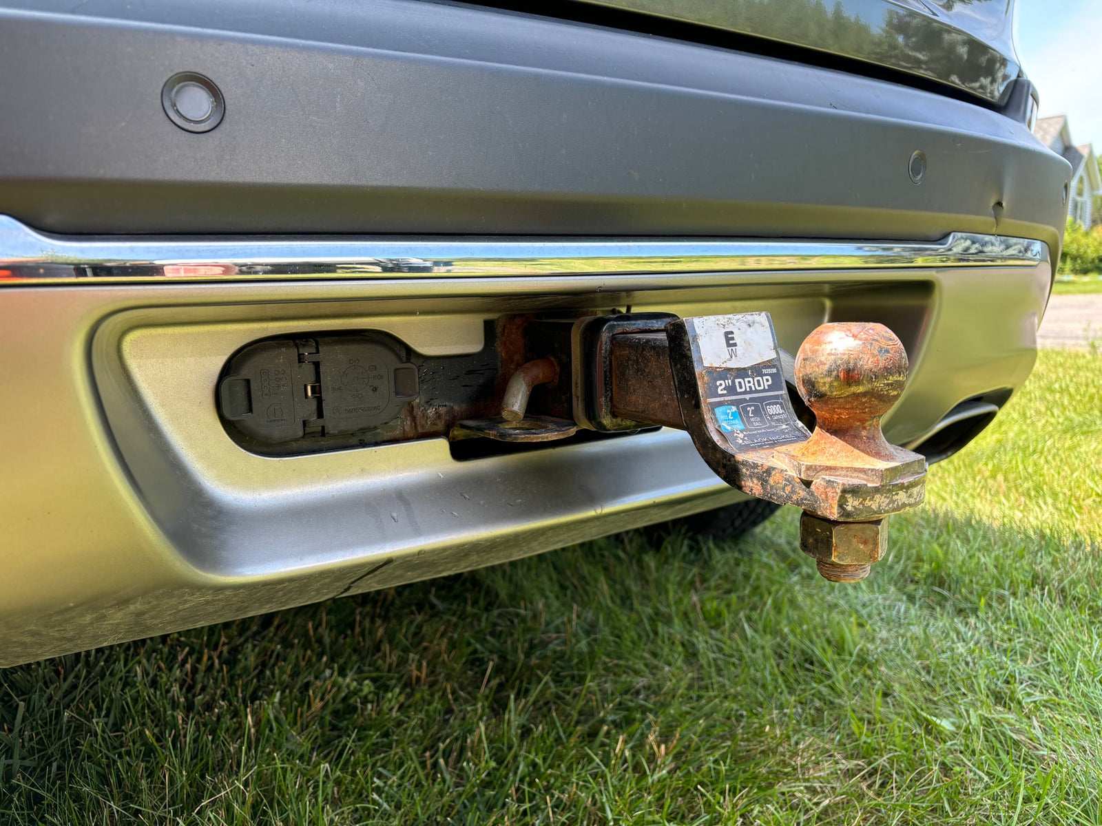 Prepped for RV rental: Vehicle rear with rusty tow hitch, electrical hookup, & parking sensors, ready for towing.