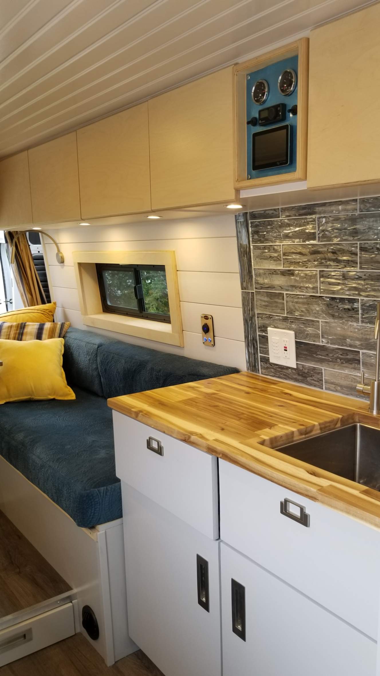 Cozy custom RV rental interior: wood cabinets, tiled kitchen, comfy blue seating, and a control panel.